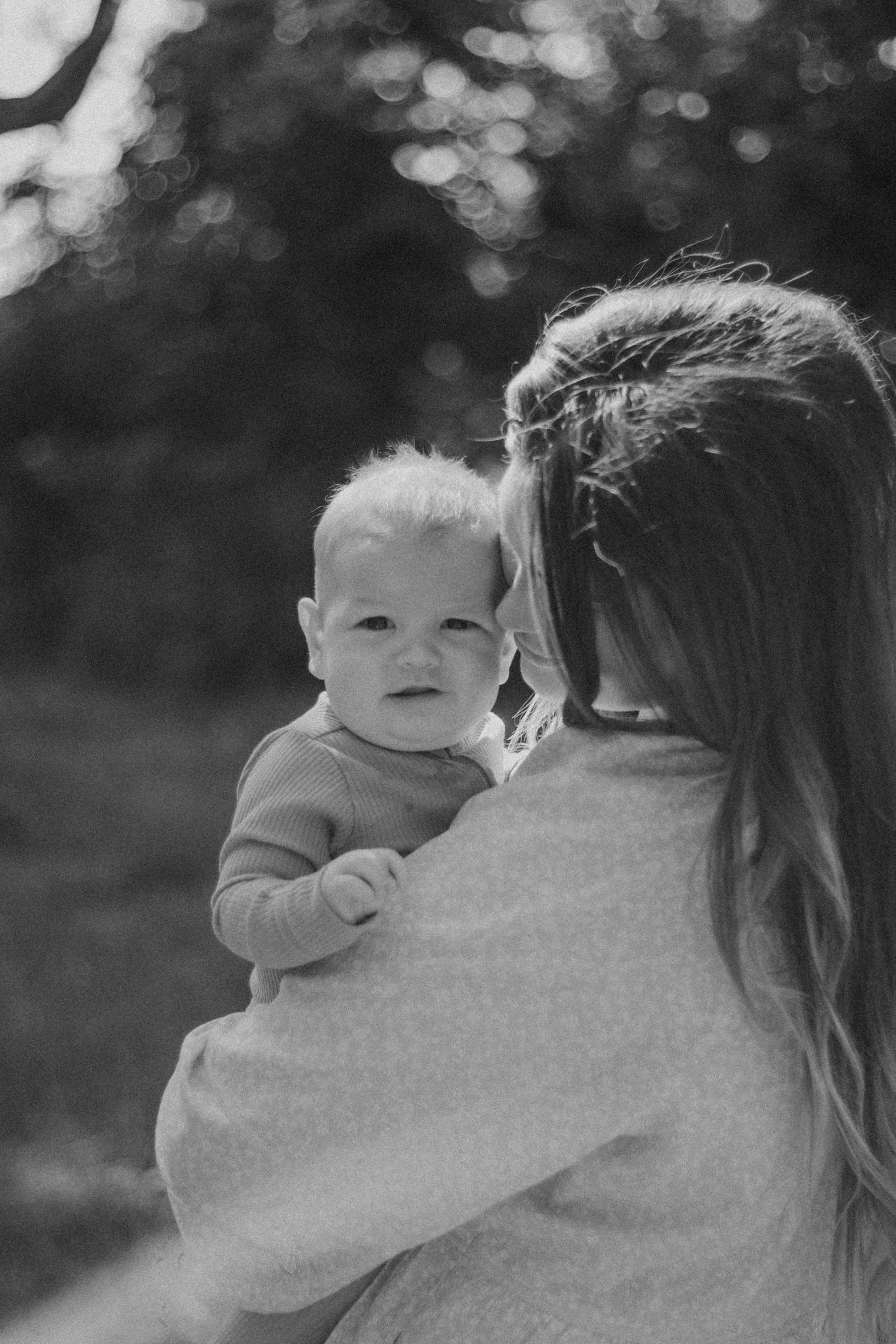 Black and white candid of mother holding baby outdoors, capturing tender connection.